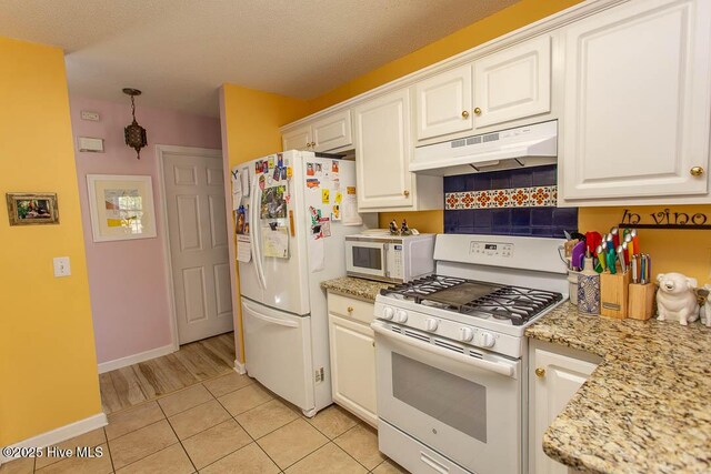 kitchen with white appliances, white cabinets, decorative backsplash, under cabinet range hood, and light tile patterned flooring