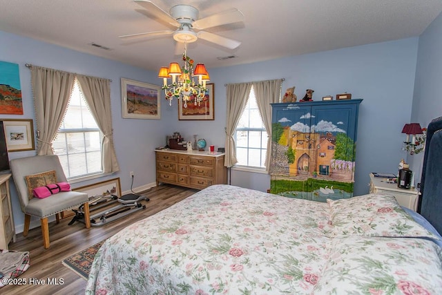 bedroom featuring baseboards, visible vents, wood finished floors, and ceiling fan with notable chandelier