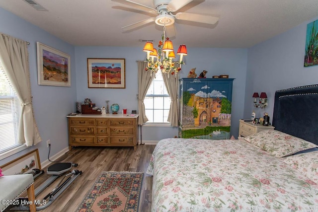 bedroom with visible vents, baseboards, wood finished floors, and ceiling fan with notable chandelier