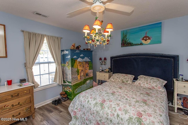 bedroom with a textured ceiling, visible vents, wood finished floors, and ceiling fan with notable chandelier