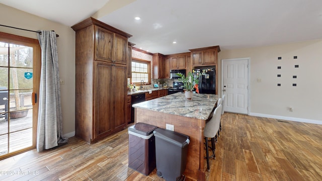 kitchen with electric stove, a kitchen bar, freestanding refrigerator, and light wood-style floors