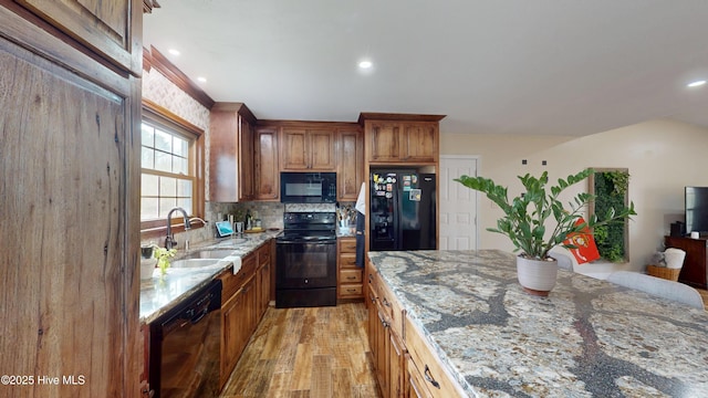 kitchen with light wood-style floors, a sink, light stone countertops, black appliances, and backsplash