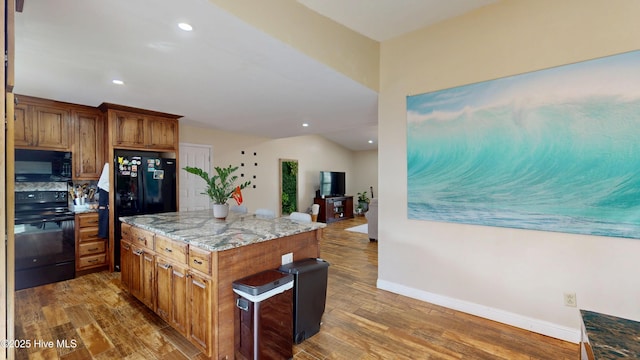 kitchen with light stone counters, wood finished floors, baseboards, brown cabinets, and black appliances