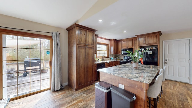 kitchen featuring tasteful backsplash, light wood-type flooring, black appliances, and light stone countertops