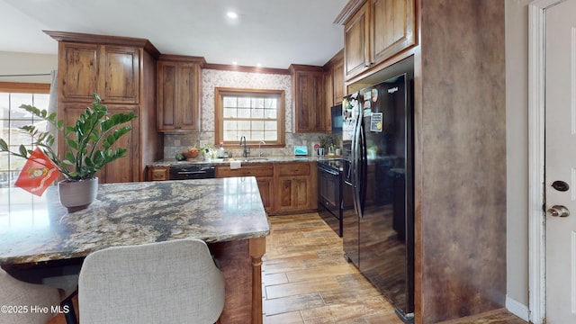 kitchen with stone countertops, brown cabinets, a sink, and black appliances