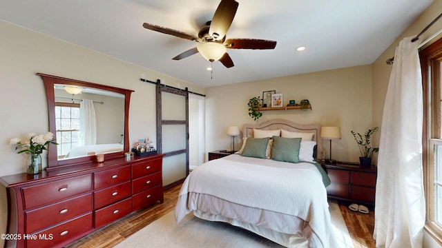 bedroom featuring ceiling fan, a barn door, wood finished floors, and recessed lighting