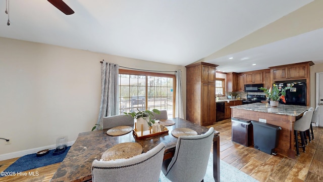 kitchen with baseboards, brown cabinetry, light wood-style flooring, a kitchen island, and black appliances