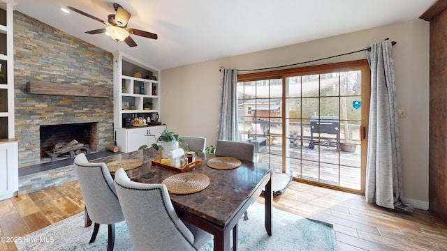 dining space with light wood-style floors, lofted ceiling, a stone fireplace, and built in shelves