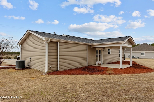 rear view of property featuring cooling unit, a yard, french doors, a shingled roof, and a patio area