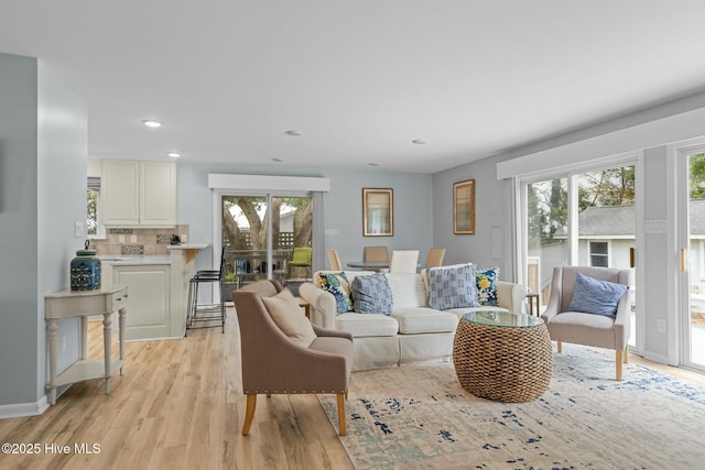 living area featuring baseboards, recessed lighting, light wood-type flooring, and a healthy amount of sunlight