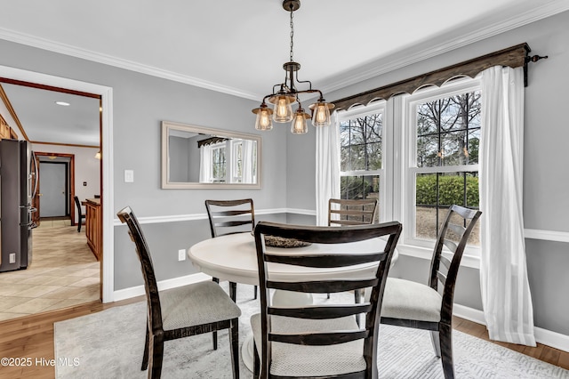 dining room with ornamental molding, an inviting chandelier, light wood-style flooring, and baseboards