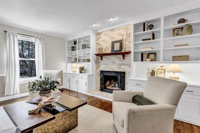 living room with built in shelves, dark wood-style flooring, a brick fireplace, and crown molding