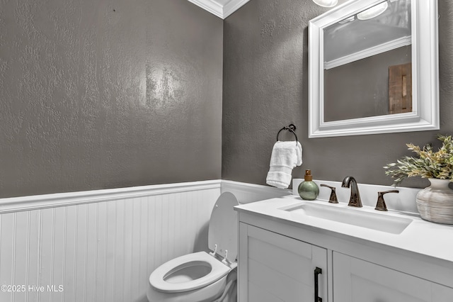 half bathroom with toilet, a textured wall, vanity, and wainscoting