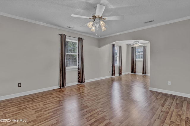 spare room with visible vents, arched walkways, wood finished floors, and ornamental molding