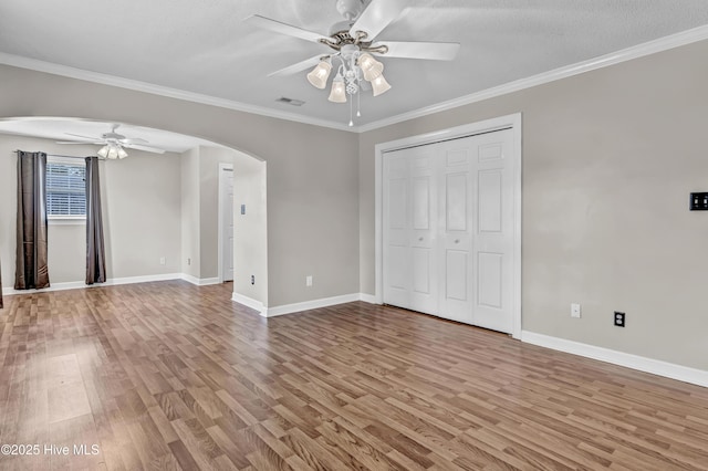 empty room featuring arched walkways, ornamental molding, wood finished floors, and visible vents