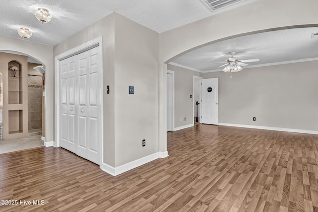 foyer entrance with arched walkways, a textured ceiling, visible vents, and light wood-style floors