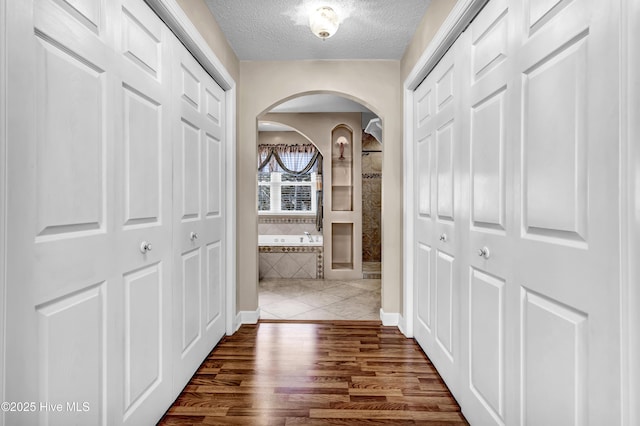 hall with arched walkways, dark wood finished floors, and a textured ceiling