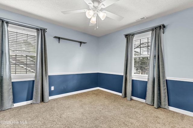 unfurnished room with a textured ceiling, ceiling fan, carpet flooring, and visible vents