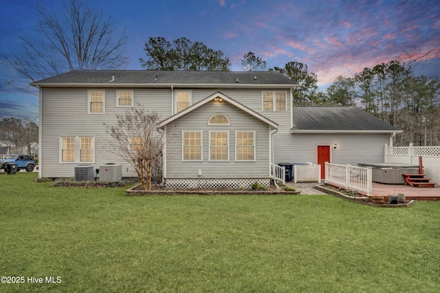 back of property at dusk featuring cooling unit, a yard, and a hot tub