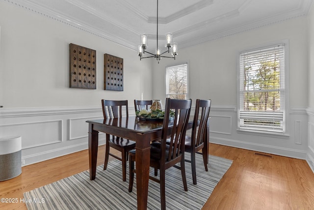 dining room with a decorative wall, wood finished floors, an inviting chandelier, a raised ceiling, and crown molding