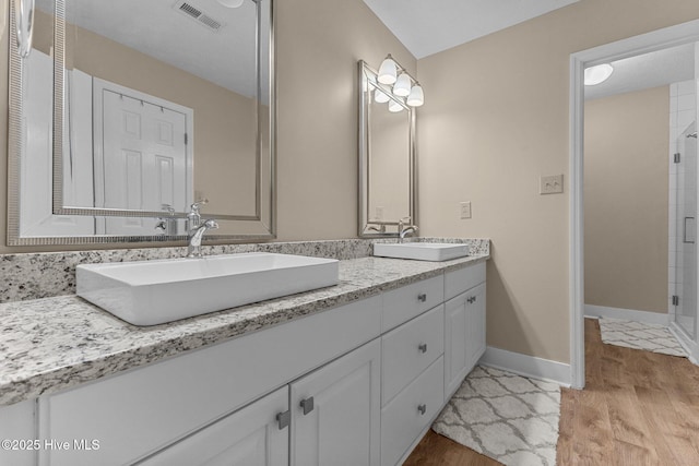 bathroom with wood finished floors, visible vents, a sink, and double vanity