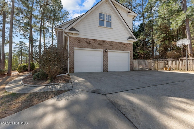 view of side of property with a garage, concrete driveway, brick siding, and fence