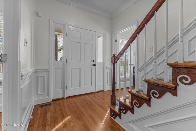 foyer with crown molding, light wood finished floors, visible vents, a decorative wall, and stairway