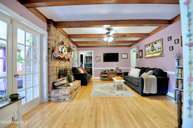 living area featuring a brick fireplace, wood finished floors, beam ceiling, and a ceiling fan