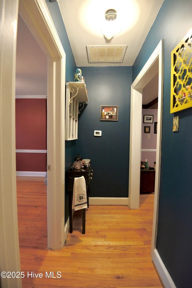 corridor featuring light wood-style floors, baseboards, and visible vents