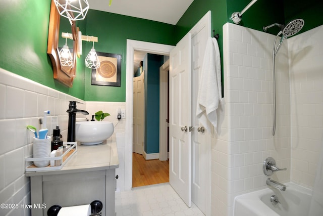 bathroom with a wainscoted wall, shower / bathtub combination, tile patterned floors, vanity, and tile walls