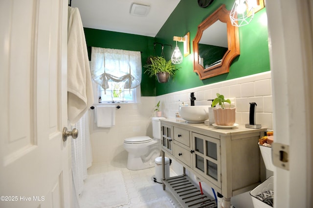 bathroom featuring wainscoting, vanity, toilet, and tile walls