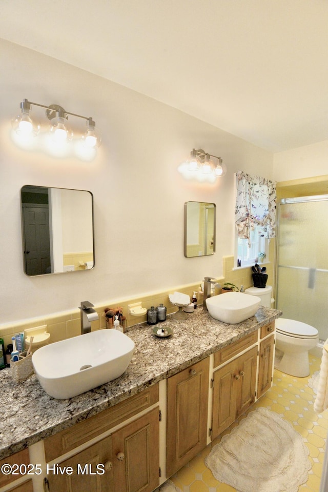 bathroom with toilet, a stall shower, double vanity, and a sink