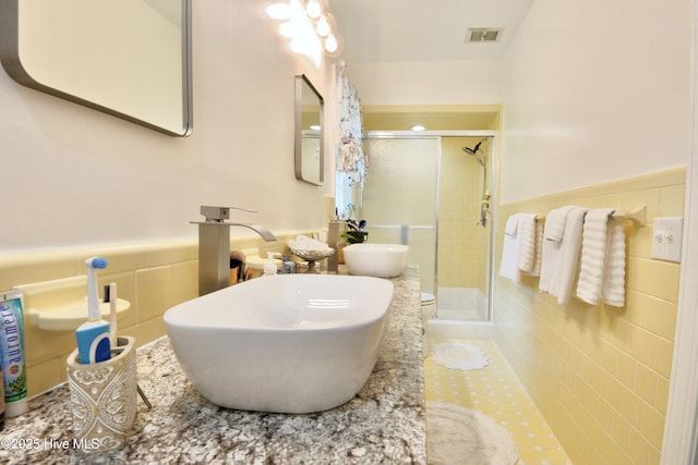 bathroom featuring a stall shower, visible vents, wainscoting, a sink, and tile walls