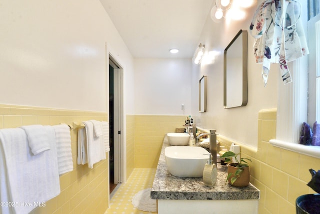 full bathroom featuring a wainscoted wall, a sink, tile walls, and double vanity