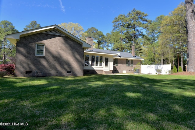 rear view of property with crawl space, a chimney, a lawn, and brick siding