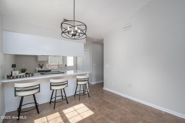 kitchen with baseboards, an inviting chandelier, a peninsula, light countertops, and a kitchen breakfast bar