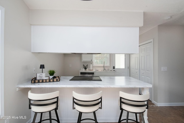 kitchen featuring white cabinets, a peninsula, a breakfast bar, and a sink