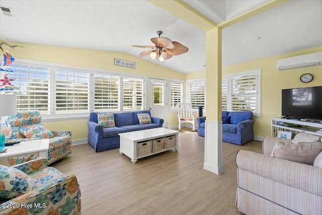 living area featuring lofted ceiling, a textured ceiling, a wall unit AC, a ceiling fan, and light wood-type flooring