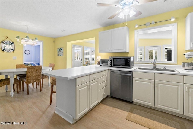 kitchen featuring appliances with stainless steel finishes, a peninsula, light countertops, light wood-style floors, and a sink