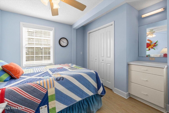 bedroom featuring a textured ceiling, ceiling fan, baseboards, a closet, and light wood-type flooring