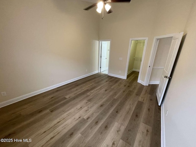 unfurnished bedroom featuring baseboards, ceiling fan, wood finished floors, a high ceiling, and a walk in closet