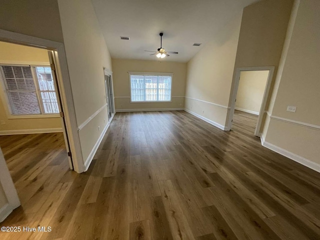 empty room featuring baseboards, visible vents, a ceiling fan, lofted ceiling, and dark wood-type flooring