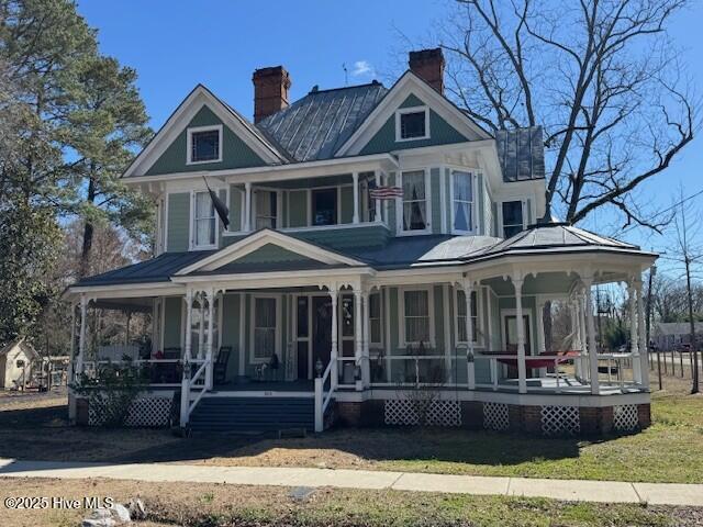 victorian house featuring a porch, a chimney, and a front lawn