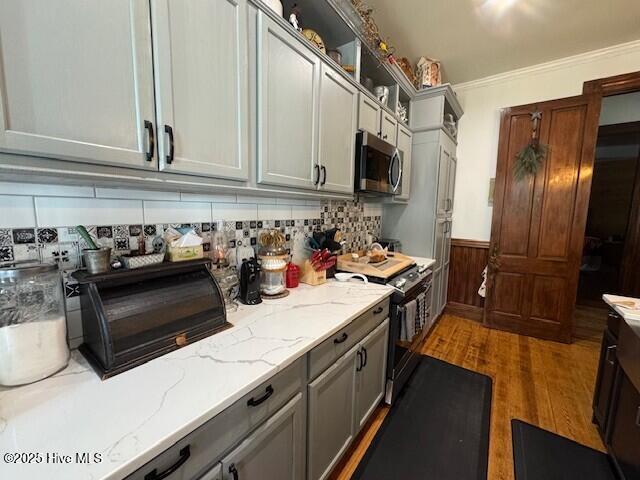 kitchen featuring light stone counters, a wainscoted wall, stainless steel appliances, ornamental molding, and dark wood-style floors