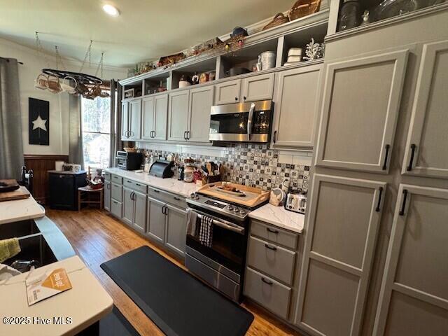 kitchen featuring light countertops, appliances with stainless steel finishes, gray cabinets, open shelves, and light wood finished floors