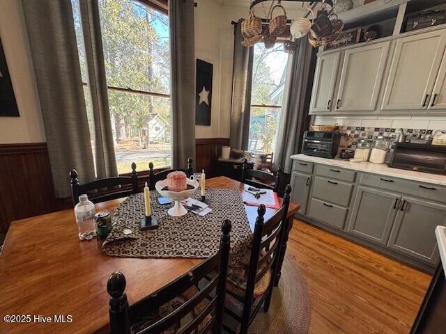 dining area with light wood-type flooring, a toaster, a wainscoted wall, and a notable chandelier