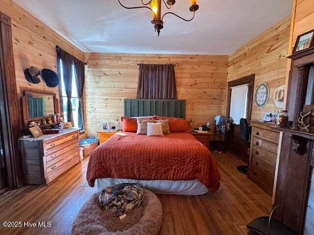 bedroom featuring wood walls, an inviting chandelier, and wood finished floors