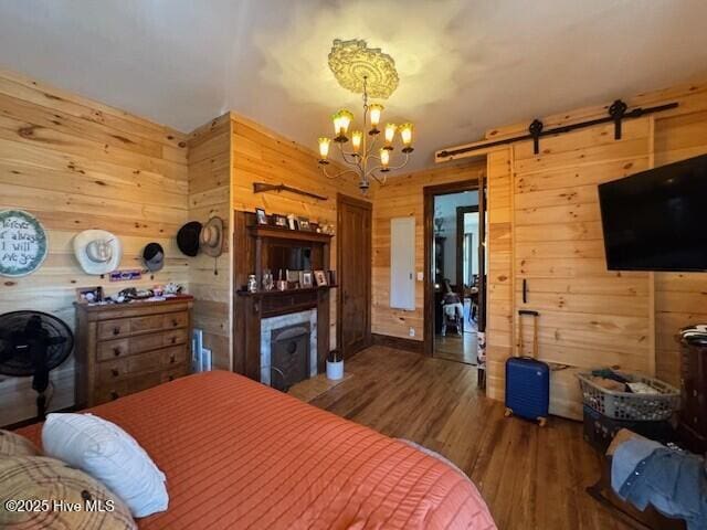 bedroom with a barn door, wooden walls, wood finished floors, a fireplace, and a notable chandelier