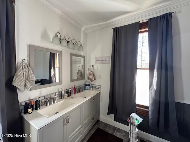 full bathroom featuring double vanity, crown molding, baseboards, and a sink