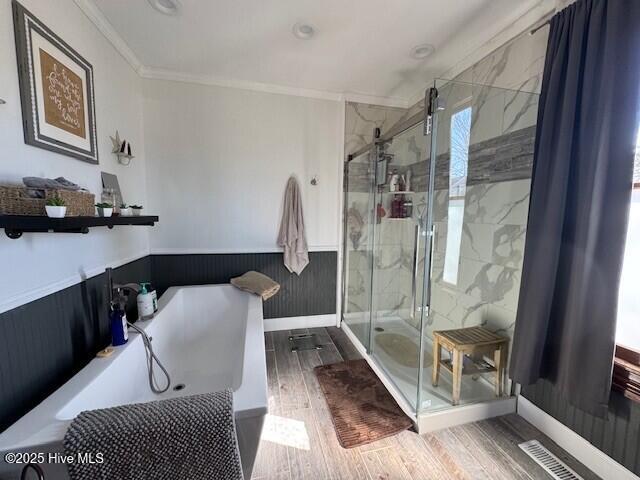 full bathroom featuring a garden tub, wood finished floors, wainscoting, a shower stall, and crown molding